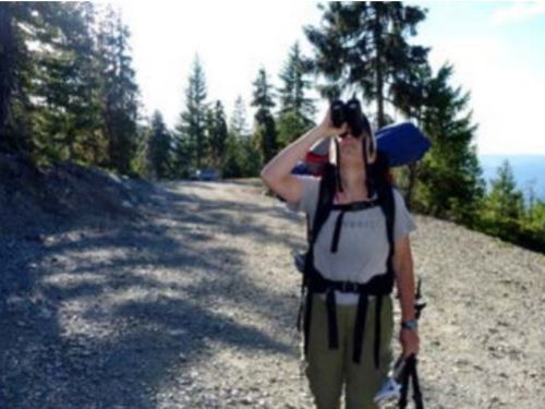 Leah Alcyon looking at conifers with binoculars at the parking lot of Devil's Punchbowl in the Siskiyou Wilderness Area, California